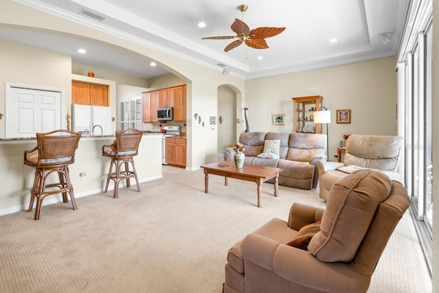 living room with ceiling fan, ornamental molding, a raised ceiling, and light carpet