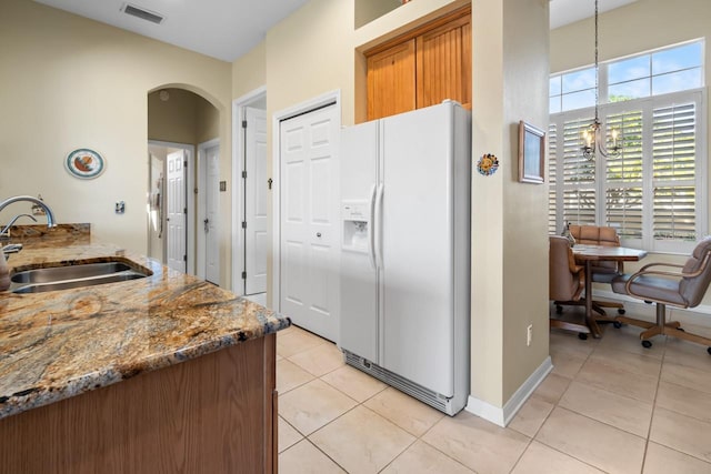 kitchen featuring sink, light tile patterned floors, hanging light fixtures, white refrigerator with ice dispenser, and a chandelier