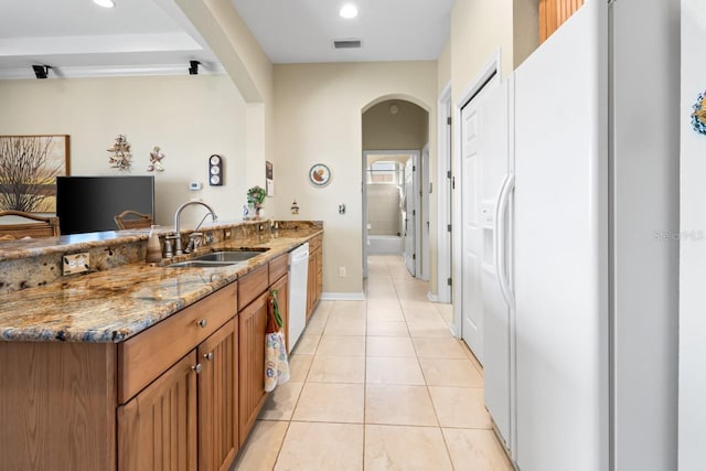 kitchen with sink, light tile patterned floors, kitchen peninsula, stone counters, and white appliances