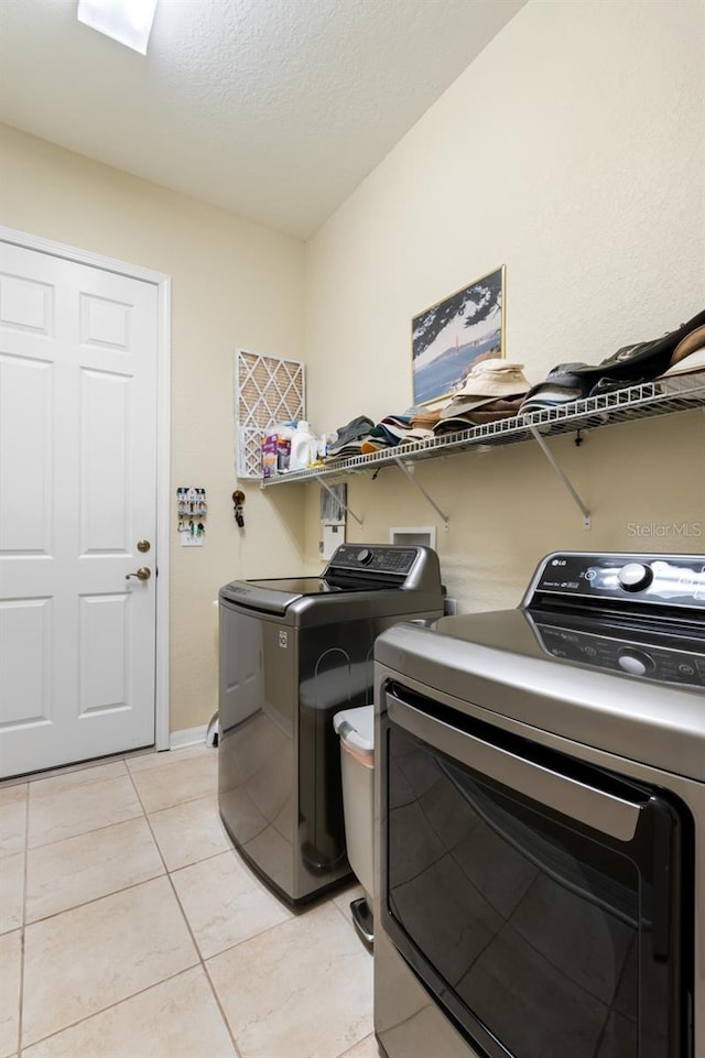 clothes washing area featuring light tile patterned floors, a textured ceiling, and independent washer and dryer