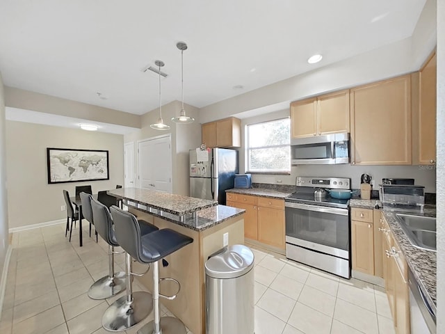 kitchen with light brown cabinetry, decorative light fixtures, a center island, light tile patterned floors, and stainless steel appliances