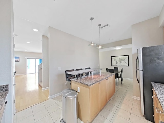 kitchen with stainless steel fridge, dark stone countertops, a kitchen island, decorative light fixtures, and light tile patterned flooring