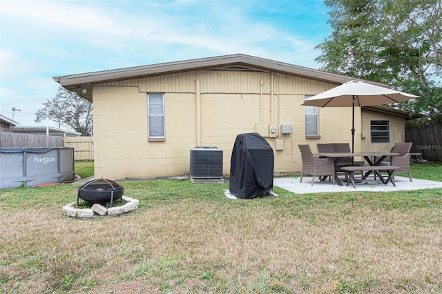 rear view of house with a patio, a yard, central AC unit, an outdoor fire pit, and a covered pool