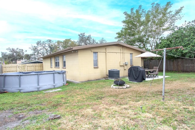 back of house featuring a covered pool, a lawn, central AC unit, and a fire pit