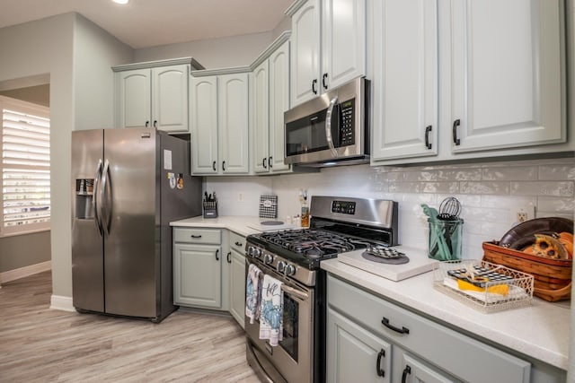 kitchen with appliances with stainless steel finishes, light hardwood / wood-style flooring, and backsplash