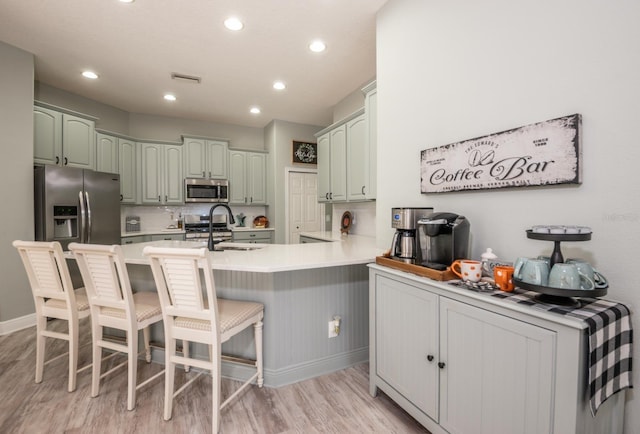 kitchen with appliances with stainless steel finishes, sink, a breakfast bar area, light hardwood / wood-style floors, and kitchen peninsula