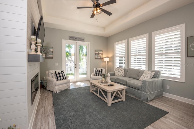 living room featuring french doors, a raised ceiling, ceiling fan, a fireplace, and hardwood / wood-style floors