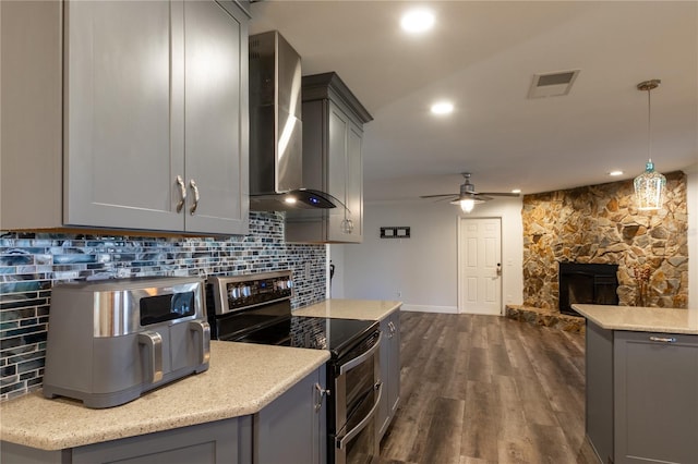 kitchen featuring decorative light fixtures, gray cabinets, wall chimney exhaust hood, and range with two ovens