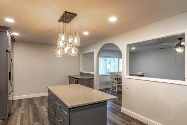 kitchen featuring pendant lighting, dark wood-type flooring, stainless steel fridge, ceiling fan, and a center island