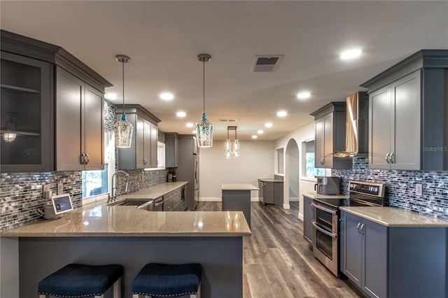 kitchen featuring sink, hanging light fixtures, double oven range, kitchen peninsula, and wall chimney range hood