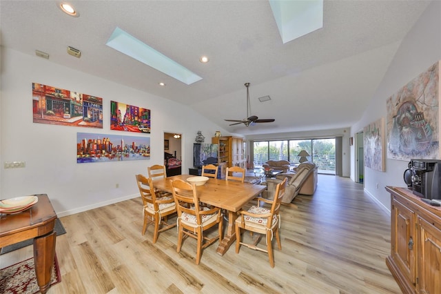 dining area with ceiling fan, a textured ceiling, vaulted ceiling with skylight, and light wood-type flooring