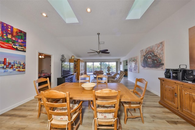 dining space featuring ceiling fan, light hardwood / wood-style flooring, and vaulted ceiling with skylight