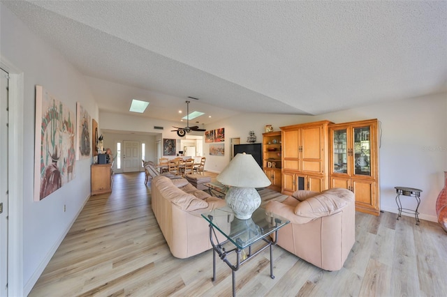 living room featuring vaulted ceiling with skylight, a textured ceiling, and light wood-type flooring