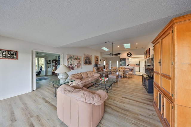 living room featuring lofted ceiling with skylight, a textured ceiling, ceiling fan, and light hardwood / wood-style floors