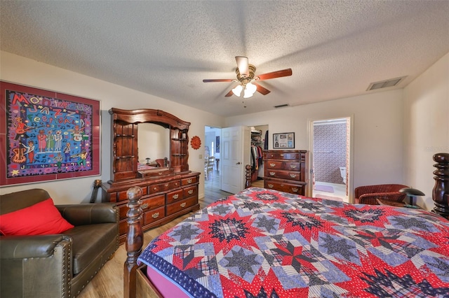 bedroom featuring connected bathroom, a walk in closet, ceiling fan, light hardwood / wood-style floors, and a textured ceiling