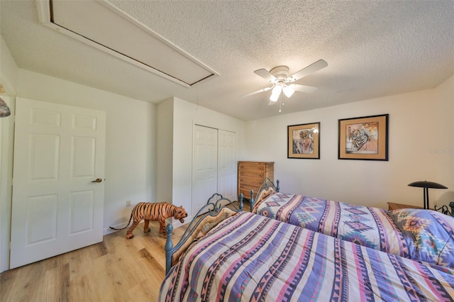 bedroom with ceiling fan, a textured ceiling, light wood-type flooring, and a closet