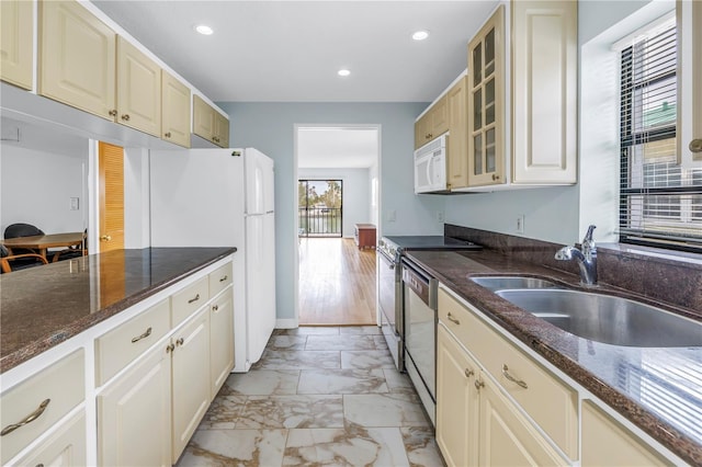 kitchen with cream cabinetry, sink, white appliances, and dark stone counters