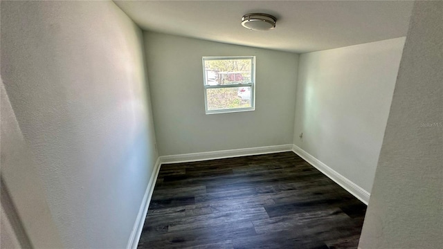 empty room with dark hardwood / wood-style flooring and vaulted ceiling