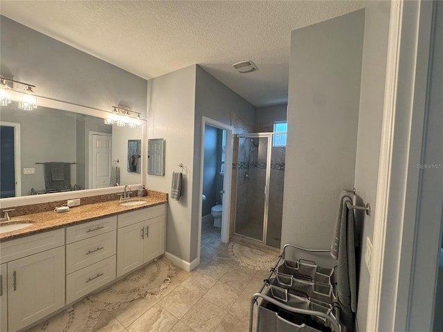 bathroom with a textured ceiling, double vanity, a sink, and a shower stall