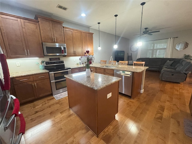 kitchen featuring stainless steel appliances, a sink, a kitchen island, open floor plan, and pendant lighting