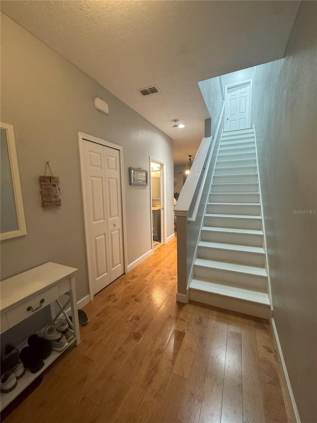 stairway with a textured ceiling, wood finished floors, visible vents, and baseboards