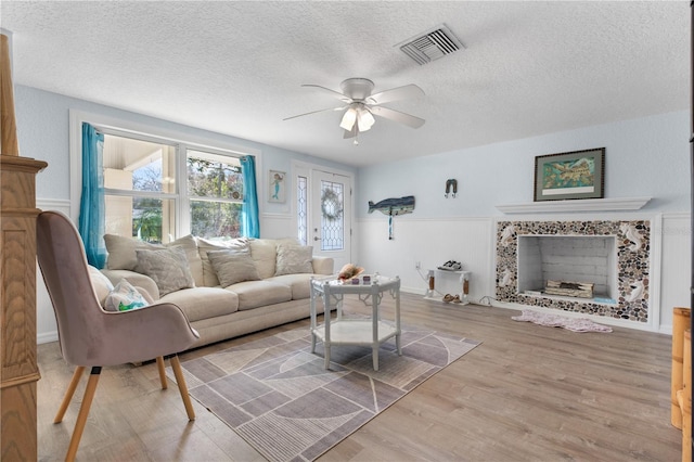 living room with ceiling fan, a premium fireplace, a textured ceiling, and light wood-type flooring