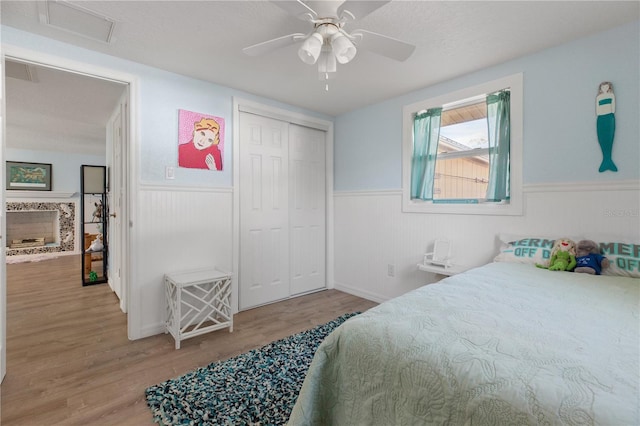 bedroom with a textured ceiling, a closet, hardwood / wood-style flooring, ceiling fan, and a high end fireplace