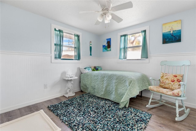 bedroom featuring a wainscoted wall, ceiling fan, and wood finished floors