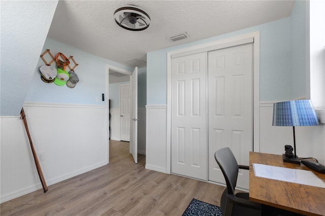 office featuring light wood-type flooring, a wainscoted wall, visible vents, and a textured ceiling