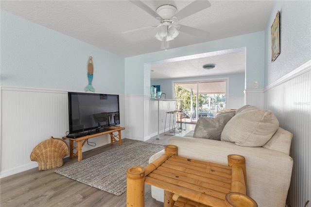 living room with a textured ceiling, ceiling fan, wainscoting, and wood finished floors