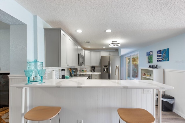 kitchen with a peninsula, appliances with stainless steel finishes, light countertops, and a kitchen breakfast bar