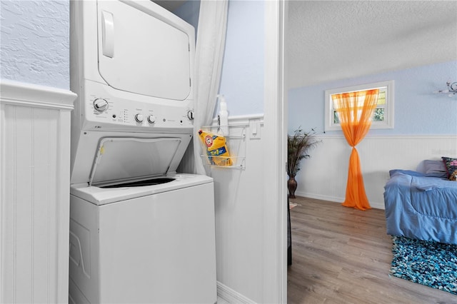 laundry room with a textured ceiling, light wood-style flooring, laundry area, stacked washer / drying machine, and wainscoting