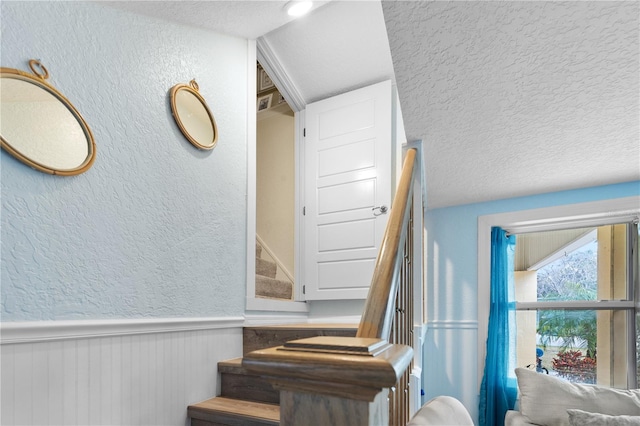 stairs featuring a textured wall, a textured ceiling, and wainscoting