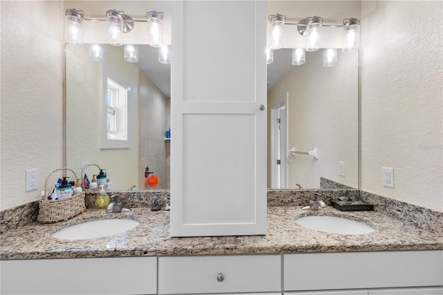 full bathroom with a textured wall, walk in shower, a sink, and double vanity