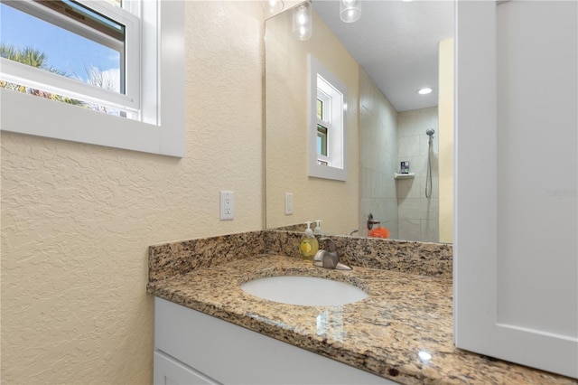 bathroom featuring a textured wall, a tile shower, and vanity