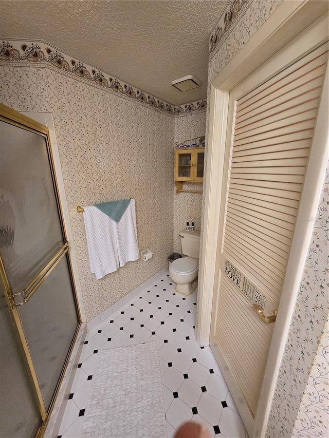 bathroom featuring toilet, a textured ceiling, and a shower with shower door