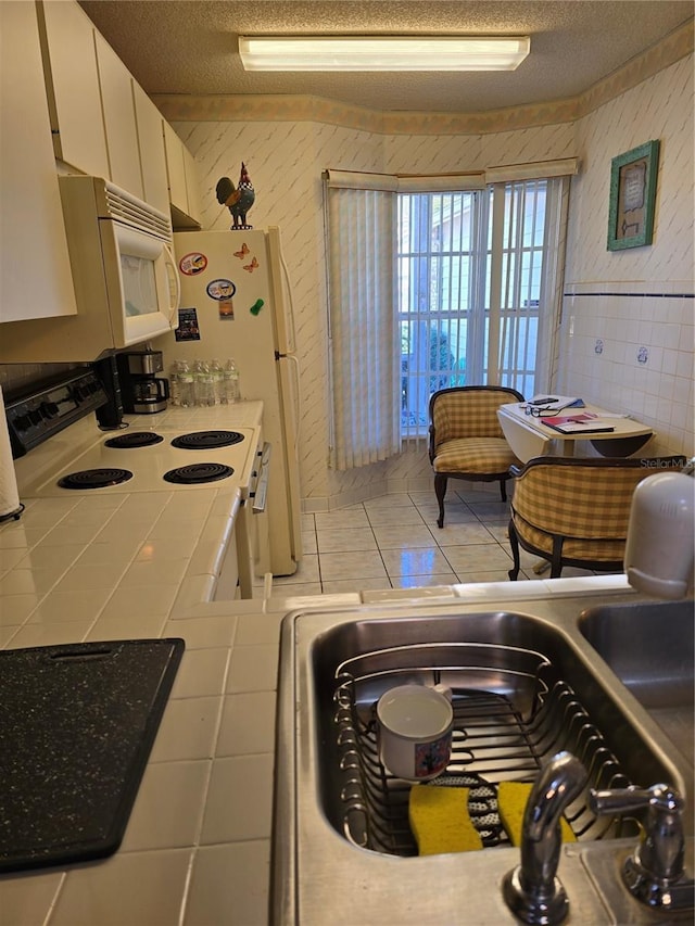 kitchen with white appliances, tile counters, a textured ceiling, and white cabinets