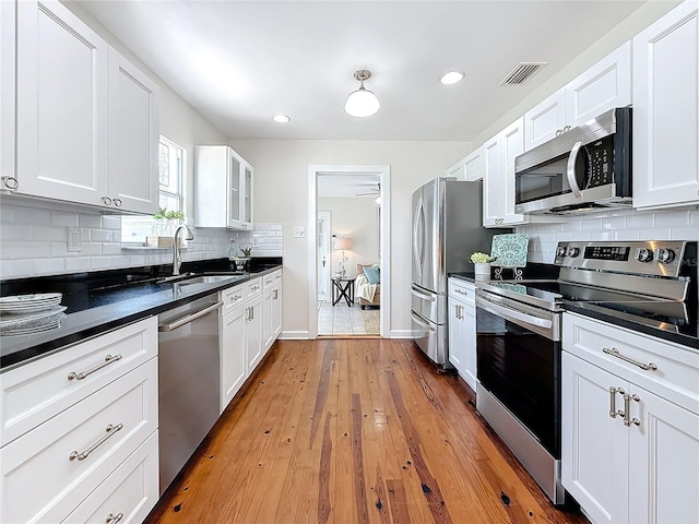 kitchen featuring sink, appliances with stainless steel finishes, white cabinets, decorative backsplash, and light wood-type flooring