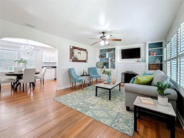 living room featuring hardwood / wood-style flooring, a fireplace, ceiling fan with notable chandelier, and built in features