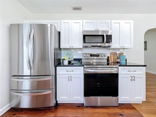 kitchen featuring appliances with stainless steel finishes, white cabinets, dark hardwood / wood-style flooring, and decorative backsplash