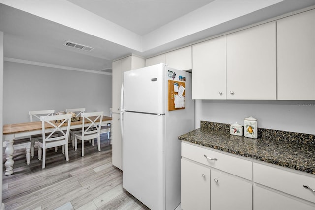 kitchen with white cabinetry, dark stone countertops, ornamental molding, white fridge, and light hardwood / wood-style floors