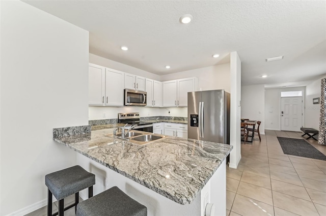 kitchen with a kitchen bar, sink, white cabinetry, kitchen peninsula, and stainless steel appliances