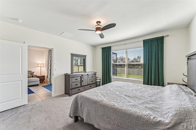 bedroom with ceiling fan, light colored carpet, and a textured ceiling