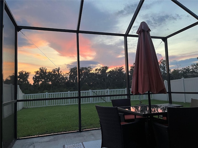 patio terrace at dusk featuring glass enclosure and a lawn