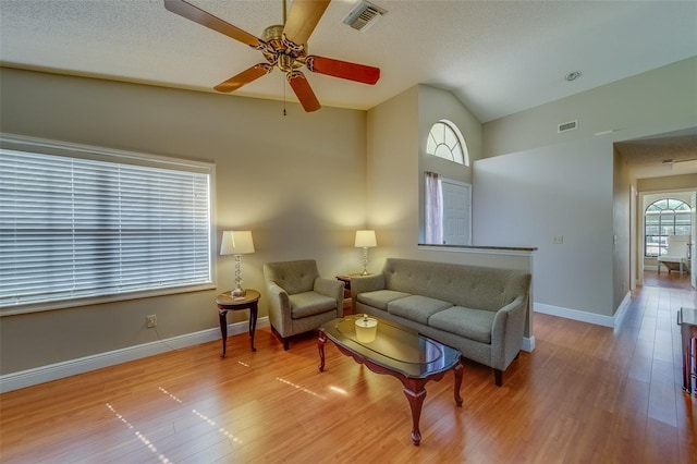 living area featuring a textured ceiling, lofted ceiling, wood finished floors, visible vents, and baseboards