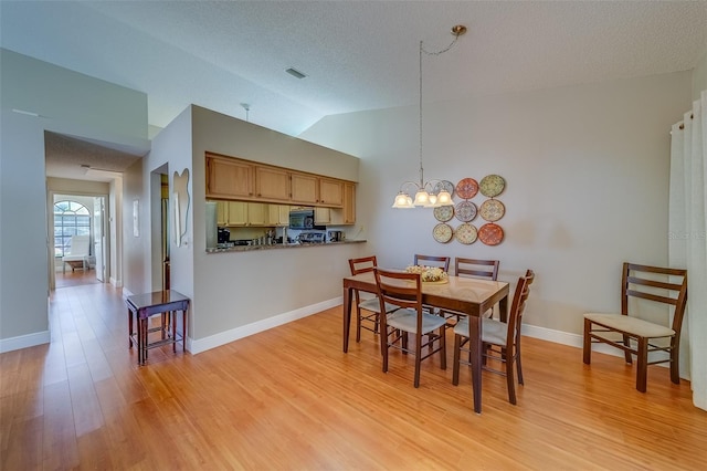 dining room with a chandelier, a textured ceiling, light wood-style flooring, baseboards, and vaulted ceiling