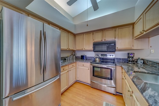 kitchen featuring dark stone counters, appliances with stainless steel finishes, light wood-type flooring, light brown cabinets, and a sink