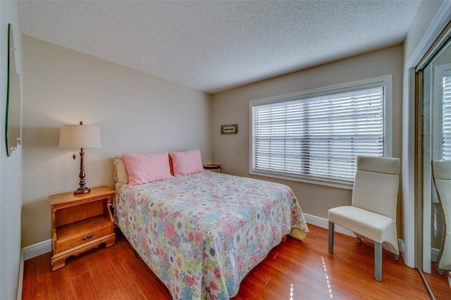 bedroom featuring a textured ceiling, a closet, wood finished floors, and baseboards