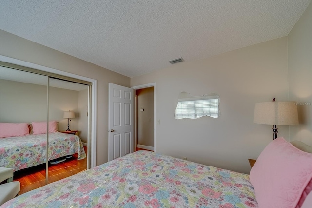 bedroom with a textured ceiling, a closet, wood finished floors, and visible vents