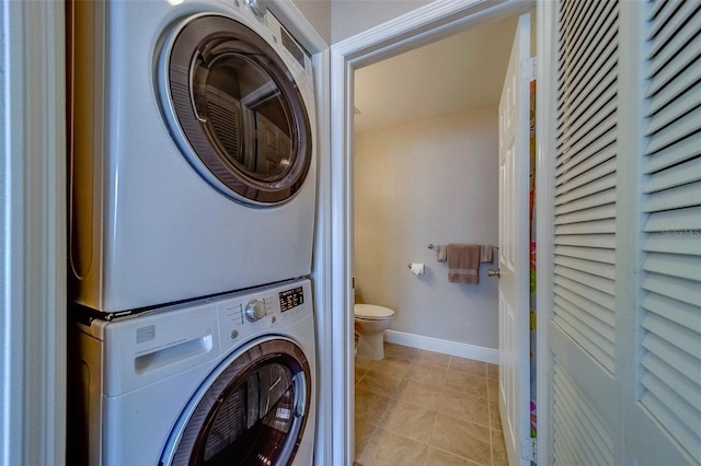 laundry room featuring baseboards, laundry area, light tile patterned flooring, and stacked washer / drying machine